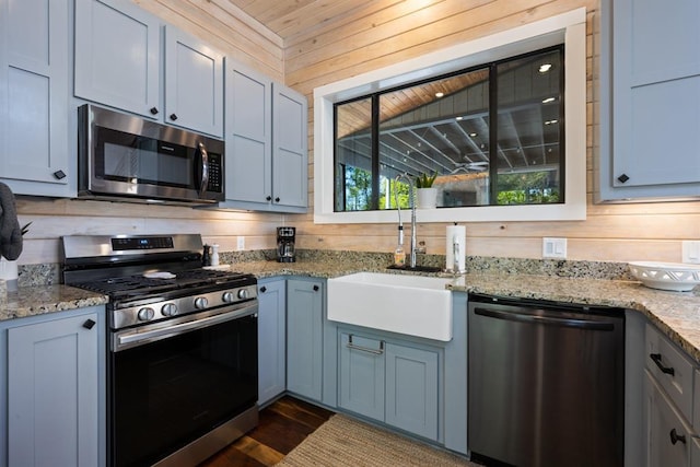 kitchen featuring a sink, stainless steel appliances, wood walls, light stone counters, and dark wood-style floors