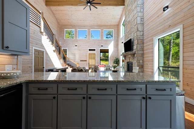 kitchen featuring gray cabinetry, light stone counters, wood walls, a peninsula, and dark wood-style floors