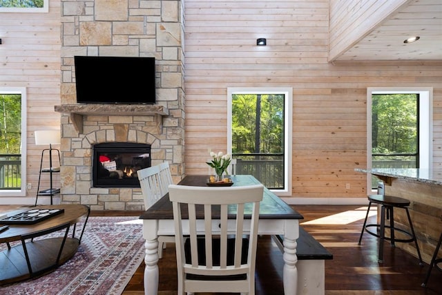 dining space featuring wood walls, dark wood-style flooring, baseboards, and a stone fireplace