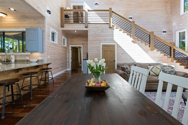 dining area with a high ceiling, dark wood-type flooring, wood walls, baseboards, and stairs