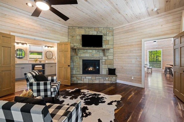 living area with wooden ceiling, dark wood-style flooring, ceiling fan, wood walls, and a fireplace