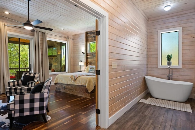 bathroom with hardwood / wood-style flooring, wood walls, a ceiling fan, a freestanding bath, and connected bathroom