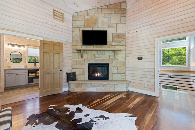 living area with a fireplace, wood walls, wood-type flooring, and high vaulted ceiling