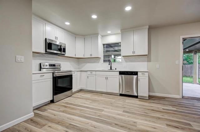 kitchen with a sink, stainless steel appliances, white cabinets, baseboards, and light countertops