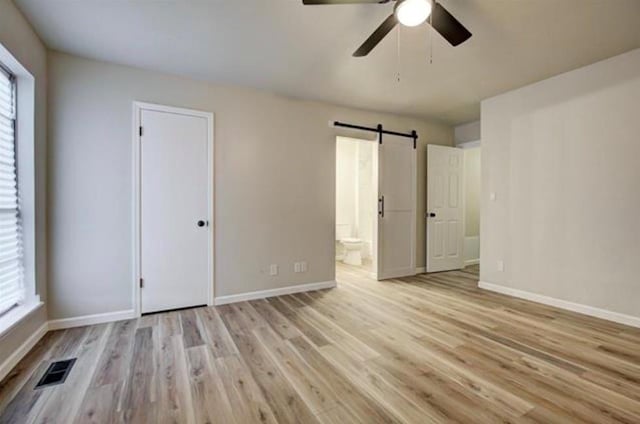 unfurnished bedroom with a barn door, baseboards, ensuite bathroom, visible vents, and wood finished floors