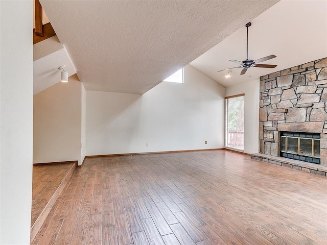 904 Carfax Rd, Edmond, OK 73034 - unfurnished living room featuring vaulted ceiling, wood finished floors, ceiling fan, a stone fireplace, and a textured ceiling
