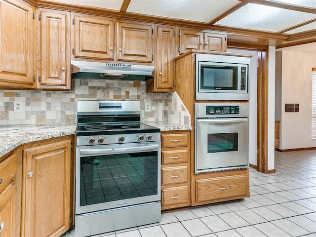 904 Carfax Rd, Edmond, OK 73034 - kitchen featuring appliances with stainless steel finishes, under cabinet range hood, tasteful backsplash, light tile patterned flooring, and light stone counters