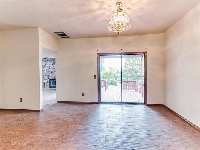 904 Carfax Rd, Edmond, OK 73034 - spare room with a chandelier, wood finished floors, a stone fireplace, and a textured ceiling