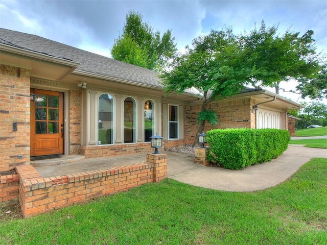 908 Carfax Rd, Edmond, OK 73034 - doorway to property featuring brick siding, a lawn, roof with shingles, and a garage