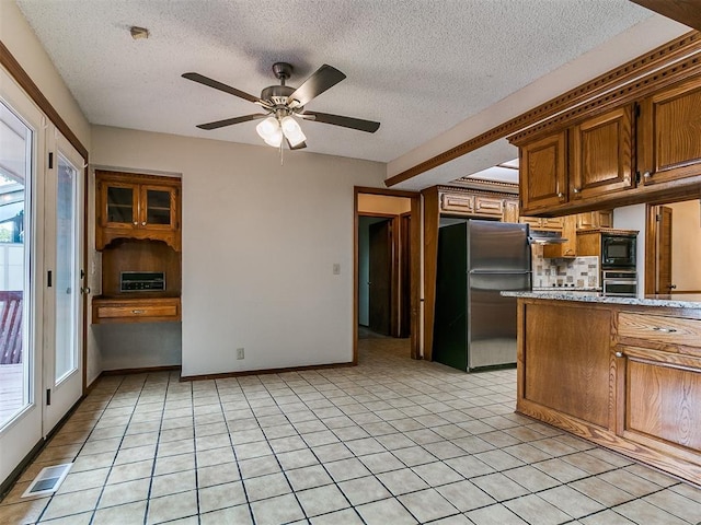 908 Carfax Rd, Edmond, OK 73034 - kitchen featuring stainless steel appliances, a ceiling fan, a textured ceiling, tasteful backsplash, and brown cabinetry