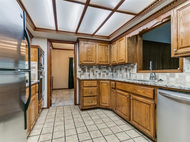 908 Carfax Rd, Edmond, OK 73034 - kitchen featuring appliances with stainless steel finishes, tasteful backsplash, brown cabinets, light stone counters, and light tile patterned floors