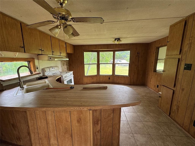 kitchen featuring a peninsula, white gas stove, a sink, ceiling fan, and wooden walls