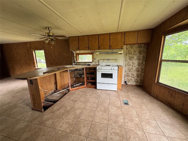 kitchen featuring white gas range, wood walls, a peninsula, and brown cabinets