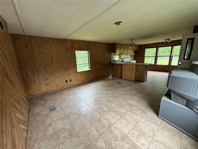 kitchen with a peninsula, wooden walls, open floor plan, and a ceiling fan