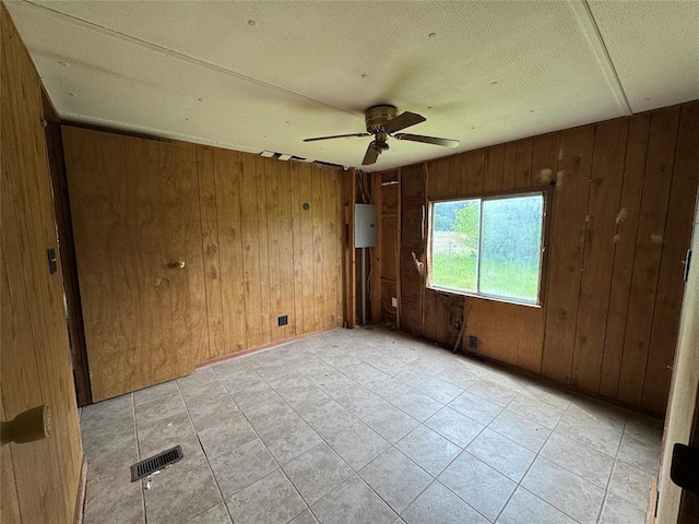 empty room with wood walls, a textured ceiling, visible vents, a ceiling fan, and light tile patterned floors