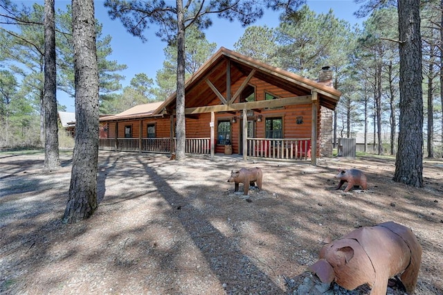view of front of home with a porch, log veneer siding, and a chimney