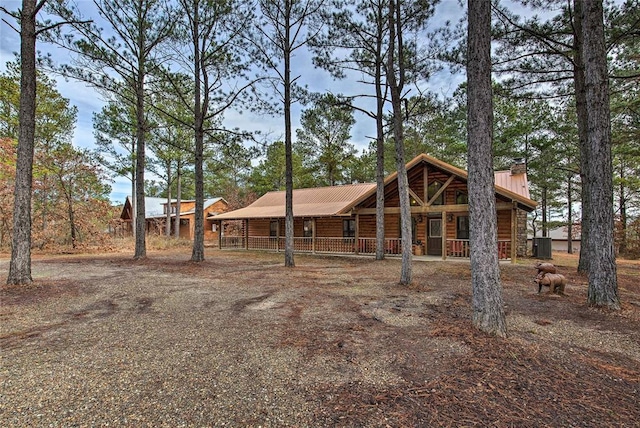view of front of property featuring covered porch, metal roof, a chimney, and log veneer siding