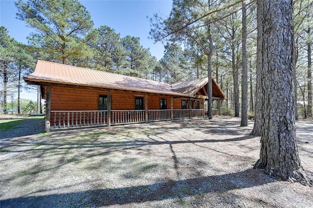 view of side of property featuring log veneer siding, a porch, metal roof, and driveway