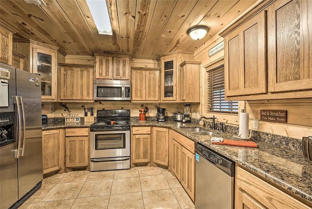kitchen featuring stainless steel appliances, a sink, wood ceiling, light tile patterned flooring, and dark stone counters