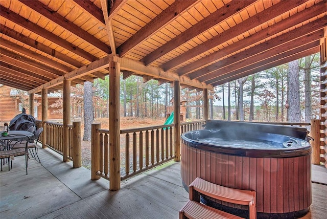 wooden terrace with a hot tub, outdoor dining space, and a playground