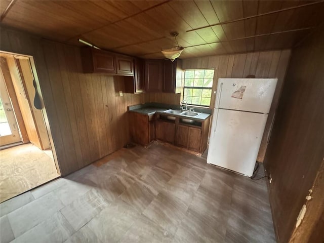 111 N 8th St, Seminole, OK 74868 - kitchen featuring freestanding refrigerator, wood walls, a sink, wood ceiling, and brown cabinets
