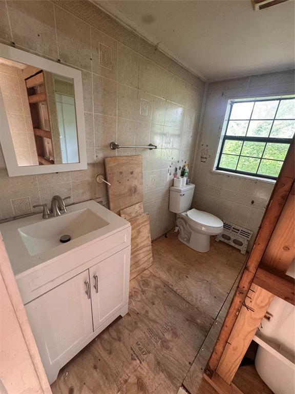 111 N 8th St, Seminole, OK 74868 - half bath with tile walls, toilet, vanity, backsplash, and wood finished floors