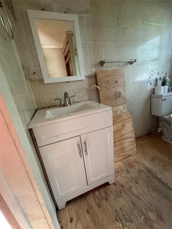 111 N 8th St, Seminole, OK 74868 - half bathroom with tile walls, backsplash, toilet, wood finished floors, and vanity