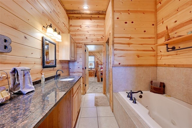 bathroom with wooden walls, vanity, a tub with jets, and tile patterned flooring