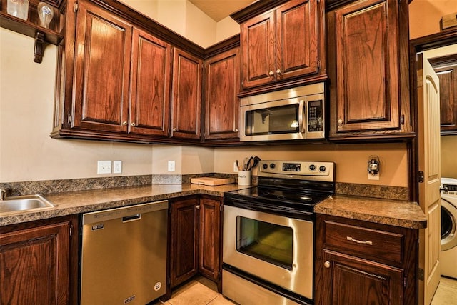kitchen with light tile patterned floors, a sink, dark countertops, washer / dryer, and appliances with stainless steel finishes