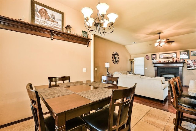 dining space featuring ceiling fan with notable chandelier, a fireplace, light tile patterned flooring, and vaulted ceiling
