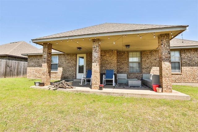 rear view of property with fence, a lawn, a shingled roof, brick siding, and a patio area