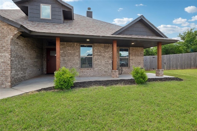 property entrance with brick siding, a patio area, a shingled roof, and a chimney