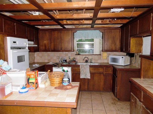 kitchen featuring white appliances, tile countertops, a sink, backsplash, and under cabinet range hood