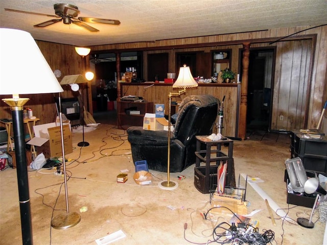 living area featuring wood walls, ceiling fan, and concrete flooring
