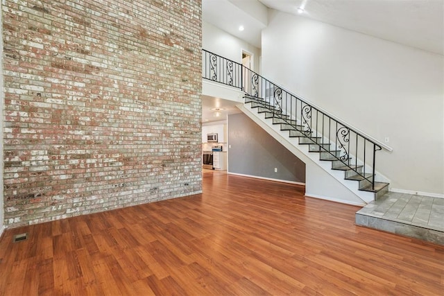 2220 NW 47th St, Oklahoma City, OK 73112 - unfurnished living room with brick wall, a towering ceiling, wood finished floors, and stairs