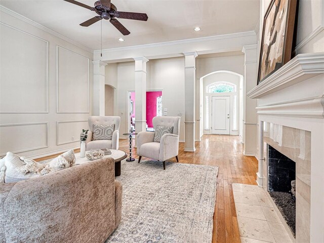 2417 Pawnee Xing, Edmond, OK 73034 - living room with ceiling fan, crown molding, light wood-style flooring, decorative columns, and a tile fireplace
