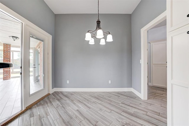 unfurnished dining area featuring light wood-style flooring, baseboards, and a notable chandelier