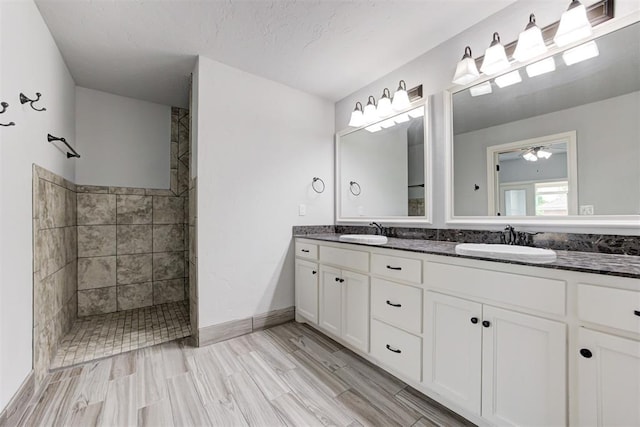 full bathroom with ceiling fan, tiled shower, double vanity, and a sink