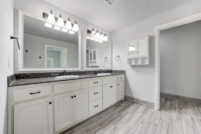 full bathroom featuring a sink, double vanity, baseboards, and wood finished floors