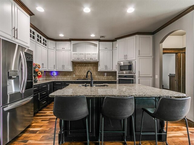 1808 Lago Dr, Moore, OK 73160 - kitchen with stainless steel appliances, a sink, arched walkways, backsplash, and light stone counters