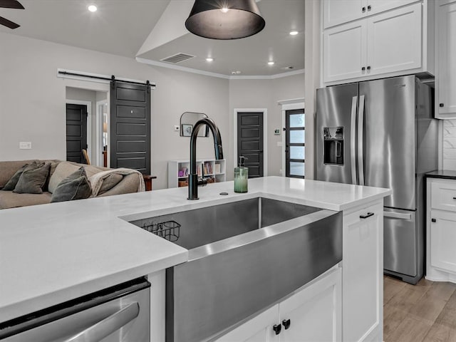 8332 Poplar Dr, Edmond, OK 73034 - kitchen with a barn door, appliances with stainless steel finishes, white cabinets, recessed lighting, and light wood finished floors