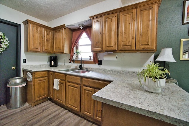 1208 Cathy Ln, Oklahoma City, OK 73110 - kitchen featuring a sink, light wood-style flooring, brown cabinetry, a textured ceiling, and light countertops