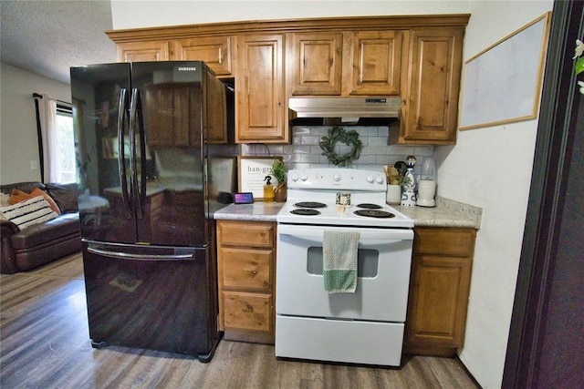 1208 Cathy Ln, Oklahoma City, OK 73110 - kitchen featuring freestanding refrigerator, electric stove, under cabinet range hood, light wood finished floors, and decorative backsplash