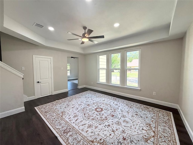 empty room with dark wood finished floors, ceiling fan, a raised ceiling, baseboards, and recessed lighting