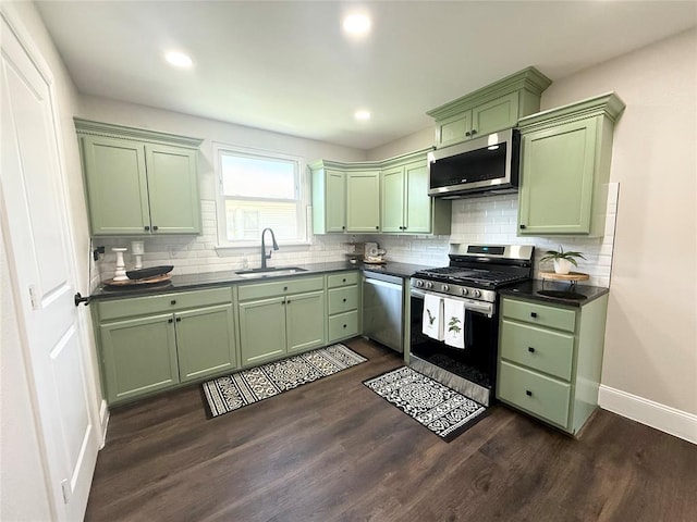 kitchen with green cabinets, appliances with stainless steel finishes, a sink, dark countertops, and recessed lighting