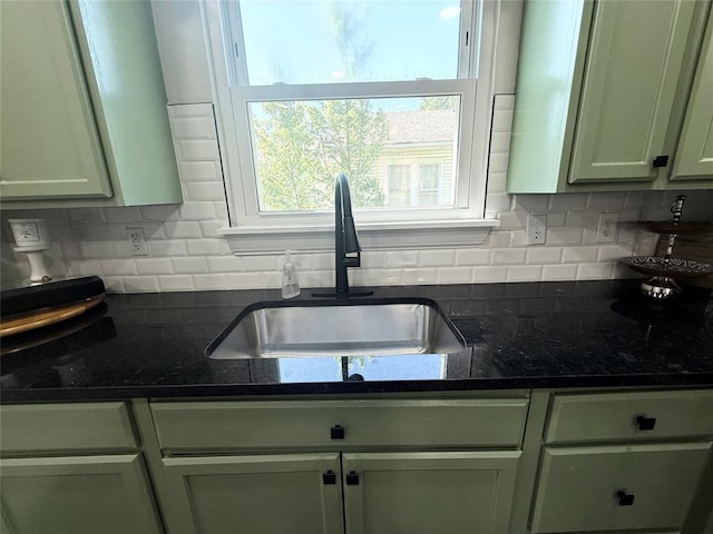 kitchen with a sink, backsplash, and dark stone countertops