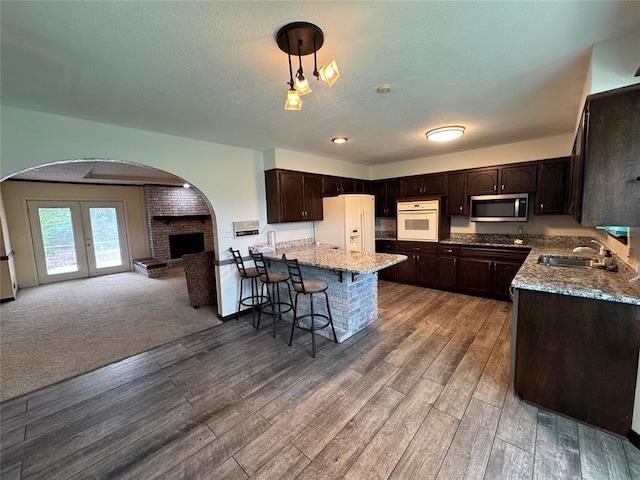 804 William Blvd, Seminole, OK 74868 - kitchen with white appliances, wood finished floors, dark brown cabinetry, open floor plan, and arched walkways