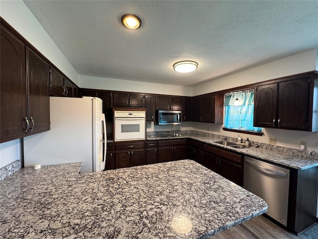804 William Blvd, Seminole, OK 74868 - kitchen featuring a sink, a peninsula, a textured ceiling, dark brown cabinets, and appliances with stainless steel finishes