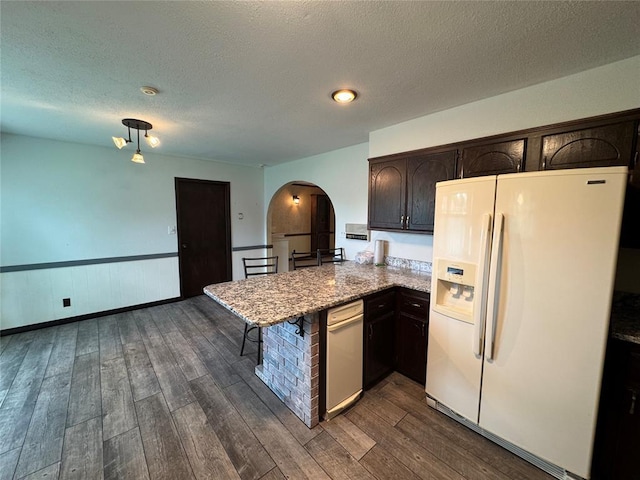 804 William Blvd, Seminole, OK 74868 - kitchen featuring a peninsula, white fridge with ice dispenser, dark brown cabinetry, arched walkways, and dark wood-style floors