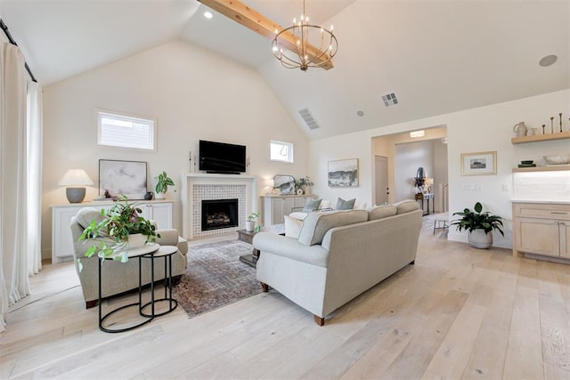 living area with high vaulted ceiling, light wood finished floors, a fireplace, and a chandelier